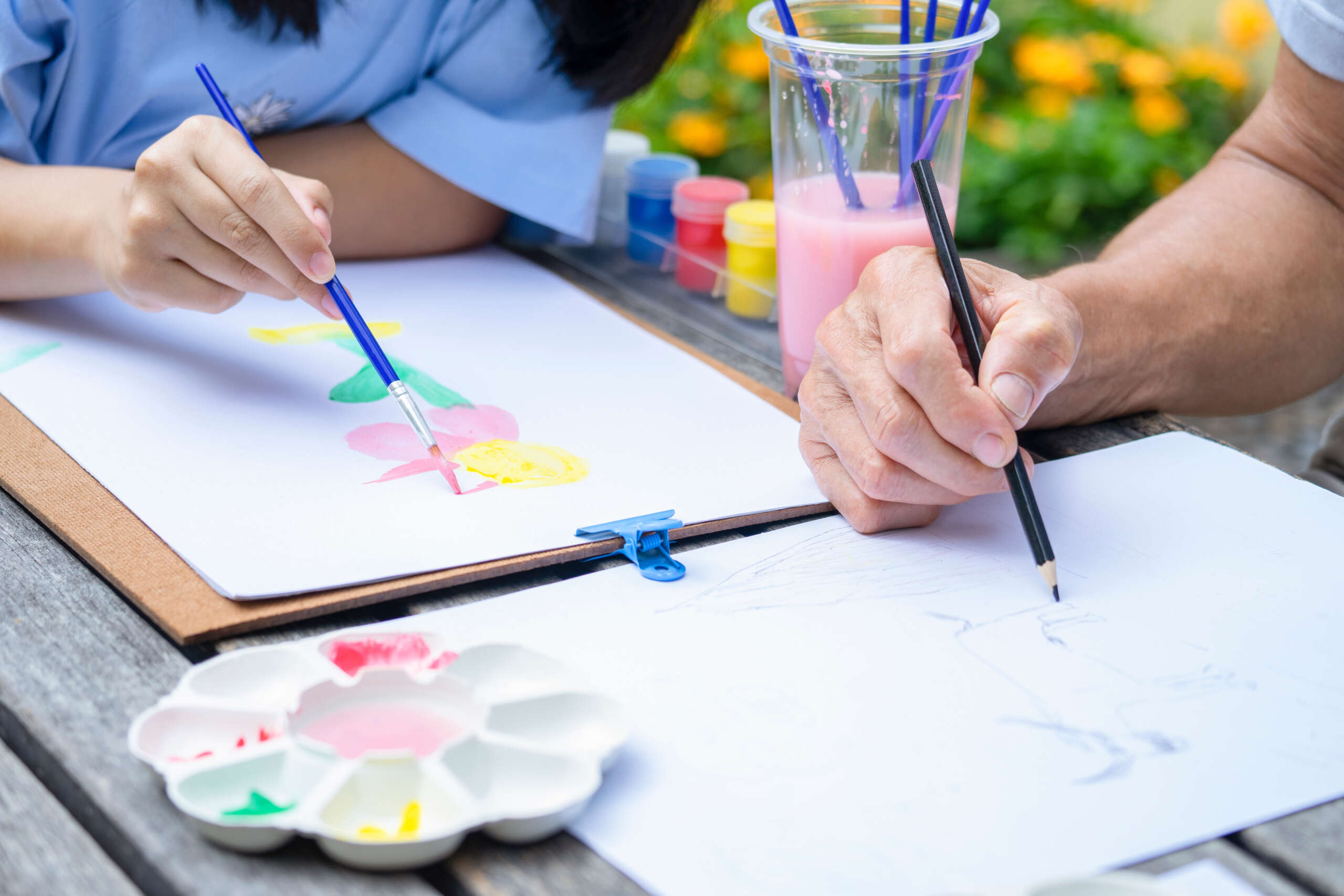 hands of teen girl painting watercolors and grandfather drawing on paper, grandfather and granddaughter spend leisure time doing artwork together