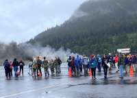 Dozens of volunteers gather with smoke and aircraft fire in the background