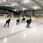 Beginning speed skaters in a crouch follow an instructor on the ice at Treadwell Arena