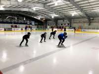 Beginning speed skaters in a crouch follow an instructor on the ice at Treadwell Arena