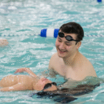 During a swim lesson, an adult helps a child float on their back in the water.