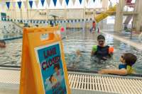 A swim instructor and two children in a pool next to a lane closed sign.