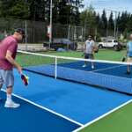 Four people holding paddles play pickleball around a net.