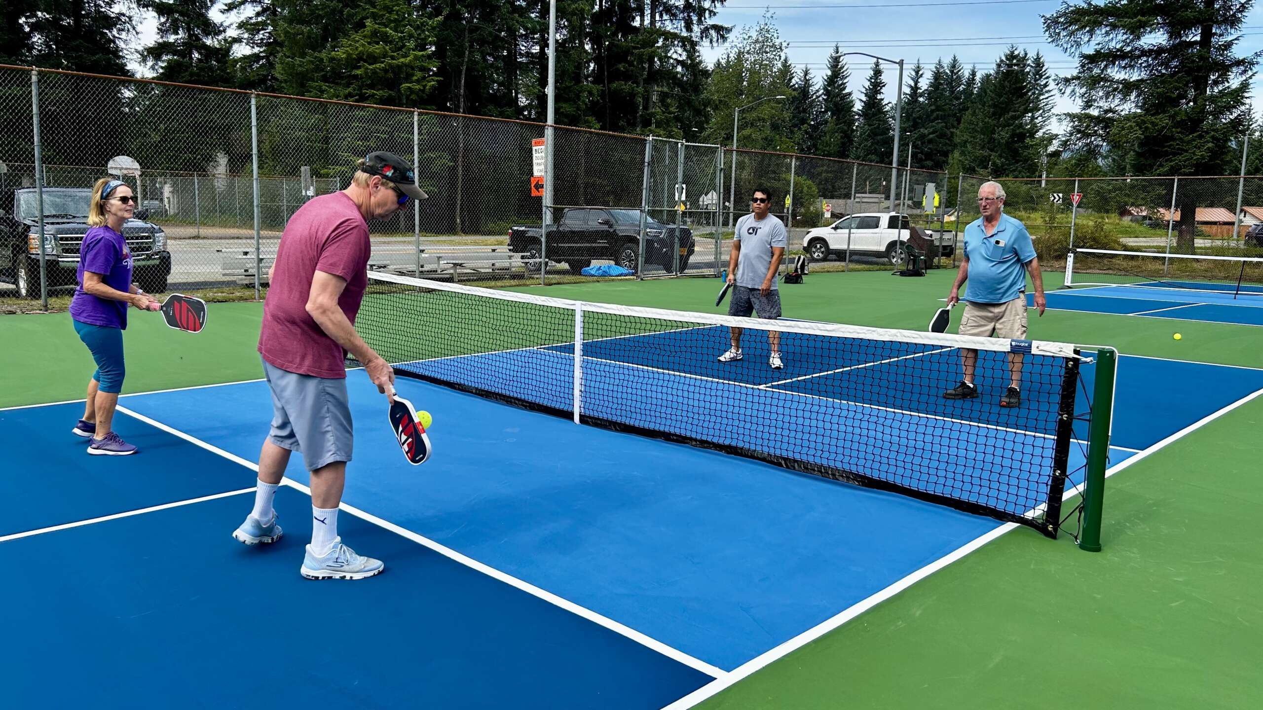 Pball 1 Four people holding paddles play pickleball around a net.