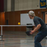 Two men play pickleball in an indoor gymnasium.