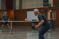 Two men play pickleball in an indoor gymnasium.