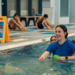 A person smiles in a pool as kids swim around her.