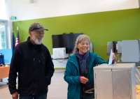 One person drops a ballot into a box as another person watches.