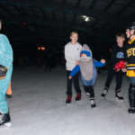 Kids wearing costumes skate on ice.